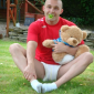 A man is sitting on the grass with Teddy and is sporting white shocks.