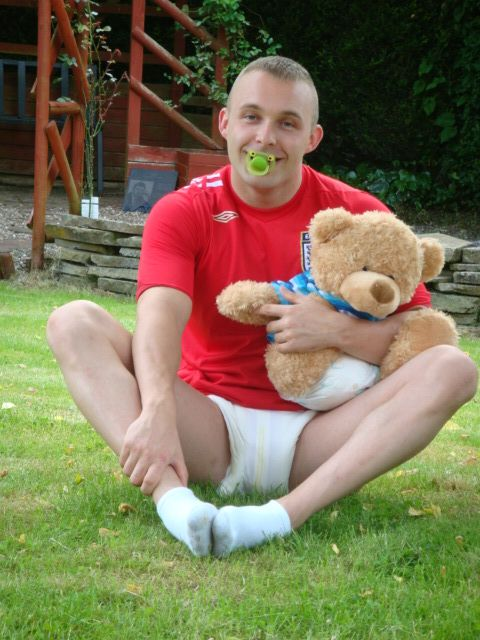 A man is sitting on the grass with Teddy and is sporting white shocks.