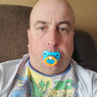 On the sofa, a man with a plain head is sucking a baby nipple while wearing a t-shirt.