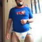 A grown man stands on the floor, saucking a baby nipple while dressed in a white diaper.