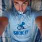 On the bed, a Suck Selfie boy is lying down. He is wearing a blue t-shirt.