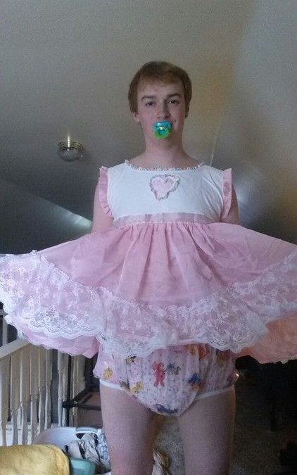He is using a Sissy Baby Diaper and appears to be a baby girl because of the white and pink dress.