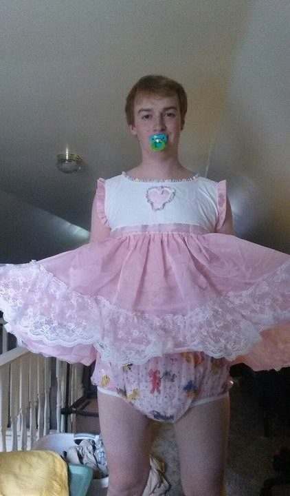 He is using a Sissy Baby Diaper and appears to be a baby girl because of the white and pink dress.