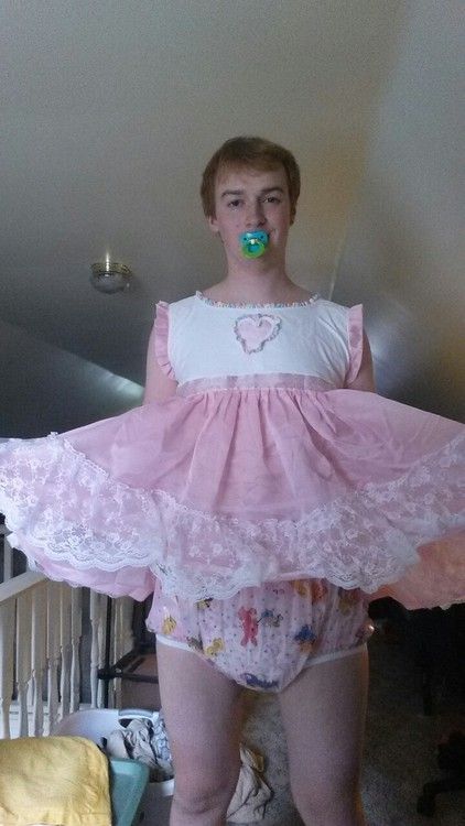 He is using a Sissy Baby Diaper and appears to be a baby girl because of the white and pink dress.